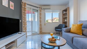 A modern living room with a flat-screen TV, a sofa with a yellow pillow, a coffee table with a bowl of cookies and a glass of orange juice, and a bookshelf.