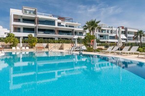 Un hôtel moderne doté d’une grande piscine, de chaises longues et de palmiers.