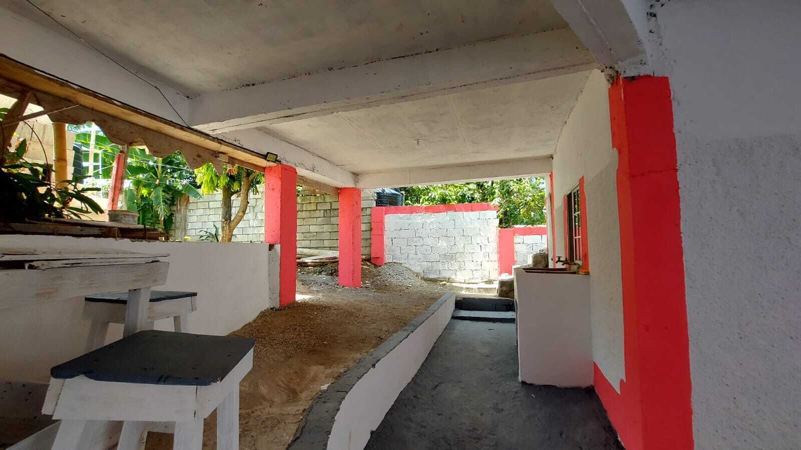 Une pièce avec un sol en béton, des murs blancs et des touches de couleur rouge. On y trouve un banc et une petite table.