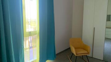 Ein Zimmer mit einem gelben Schaukelstuhl, einem weißen Kleiderschrank und einem Fenster mit blauen Vorhängen.