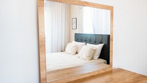 A bedroom with a large mirror, a bed with white bedding, and a wooden headboard. - Narcissos 'Nissi Beach' Apartment E9 (Ayia Napa)