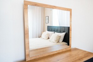 A bedroom with a large mirror, a bed with white bedding, and a wooden headboard.