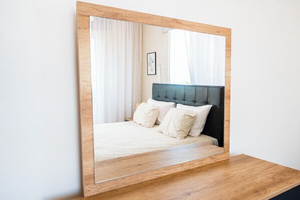 A bedroom with a large mirror, a bed with white bedding, and a wooden headboard.