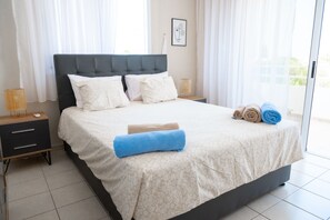 Un lit bien fait, avec une couvre-lit à motifs, deux oreillers et des serviettes enroulées posées sur une table de chevet.