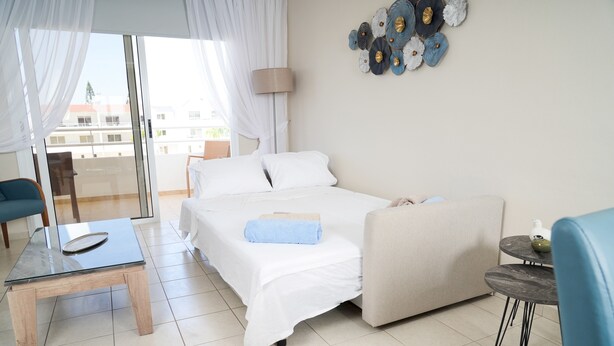 A hotel room with a bed, a small table, a sofa, and a balcony with a view. - Narcissos 'Nissi Beach' Apartment E9 (Ayia Napa)