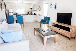 Un salon moderne avec un canapé, une table basse, un téléviseur et une cuisine en arrière-plan.