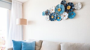 A living room with a beige sofa, two blue pillows, and a wall art piece. - Narcissos 'Nissi Beach' Apartment E9 (Ayia Napa)