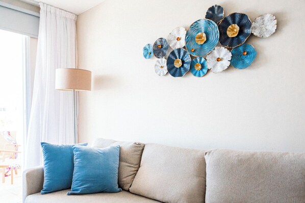 Ein Wohnzimmer mit einem beigen Sofa, zwei blauen Kissen und einem Wandbild.