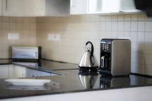 A modern kitchen with a stainless steel kettle, a coffee maker, and a toaster on the counter.