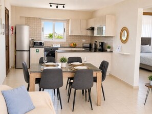 A modern kitchen with a dining area, a refrigerator, a microwave, a coffee maker, and a window with a view.