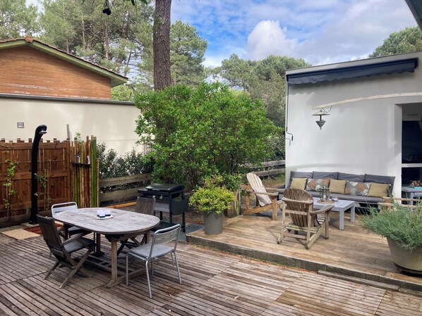 A patio with a round table and chairs, a barbecue grill, a wooden deck, and a seating area with a sofa and chairs.