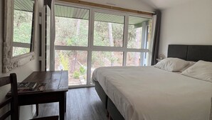 A bedroom with a large window, a bed, a desk with a chair, and a mirror. - Sweet moment in the pines  (Lacanau)