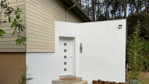 A white exterior wall with a door, a mailbox, and a small garden area with steps leading to the door. - Sweet moment in the pines  (Lacanau)