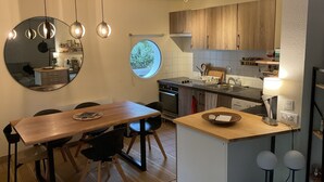 A modern kitchen with wooden cabinets, a dining table with chairs, a round mirror, and pendant lights. - Sweet moment in the pines  (Lacanau)