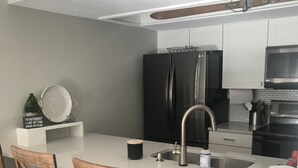 Uma cozinha moderna com armários brancos, geladeira preta, eletrodomésticos de aço inoxidável e cadeiras de madeira.