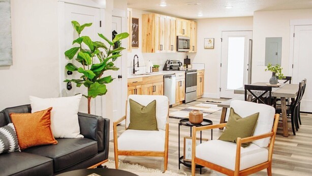 Una sala de estar moderna con un sofá negro, dos sillas de madera, una mesa de centro y una planta verde grande.