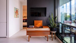 Una sala de estar moderna con un televisor de pantalla plana montado en una pared oscura, un banco de madera con libros y una planta en maceta.