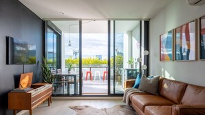 Un salón moderno con sofá de cuero, un escritorio de madera y un patio balcón con puerta corrediza de vidrio.