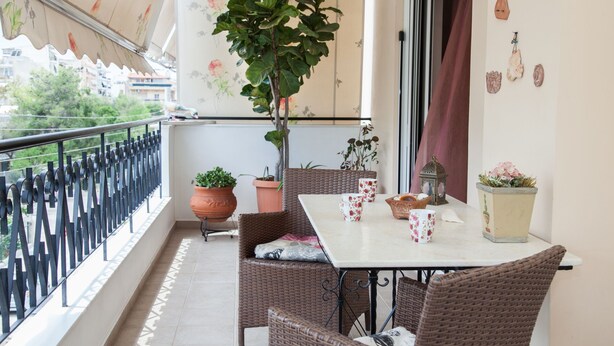 A balcony with wicker furniture, potted plants, and a table with floral cups. - Deluxe 2 Bedroom apt in Petroupoli (Petroupoli)