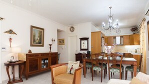A dining area with a wooden table, chairs, a chandelier, and a kitchen in the background. - Deluxe 2 Bedroom apt in Petroupoli (Petroupoli)