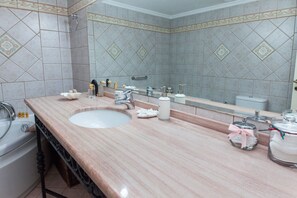 Un baño con lavamanos de mármol, un espejo grande y un inodoro.