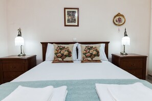 Una cama bien hecha con almohadillas florales, dos mesitas de noche con lámparas y un cuadro en la pared.