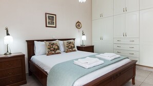 A bedroom with a wooden bed, white bedding, two bedside lamps, a large wardrobe, and a framed picture on the wall. - Deluxe 2 Bedroom apt in Petroupoli (Petroupoli)