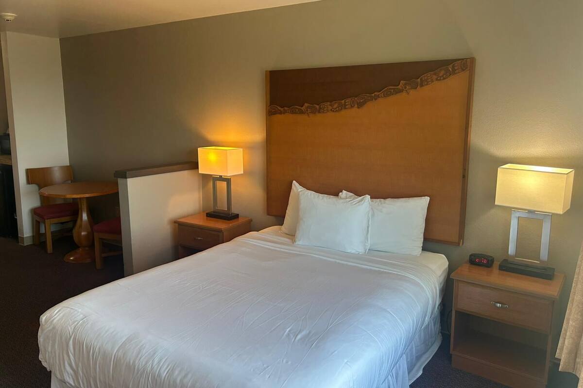 A hotel room with a large bed, two bedside tables with lamps, a wooden headboard, and a small desk with a chair.