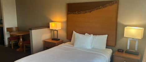 A hotel room with a large bed, two bedside tables with lamps, a wooden headboard, and a small desk with a chair.