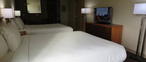 Habitación de hotel con dos camas, televisión y escritorio con lámpara.