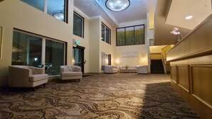 Un vestíbulo amplio con alfombra estampada, zona de estar con sofás y una escalera que conduce a los pisos superiores.