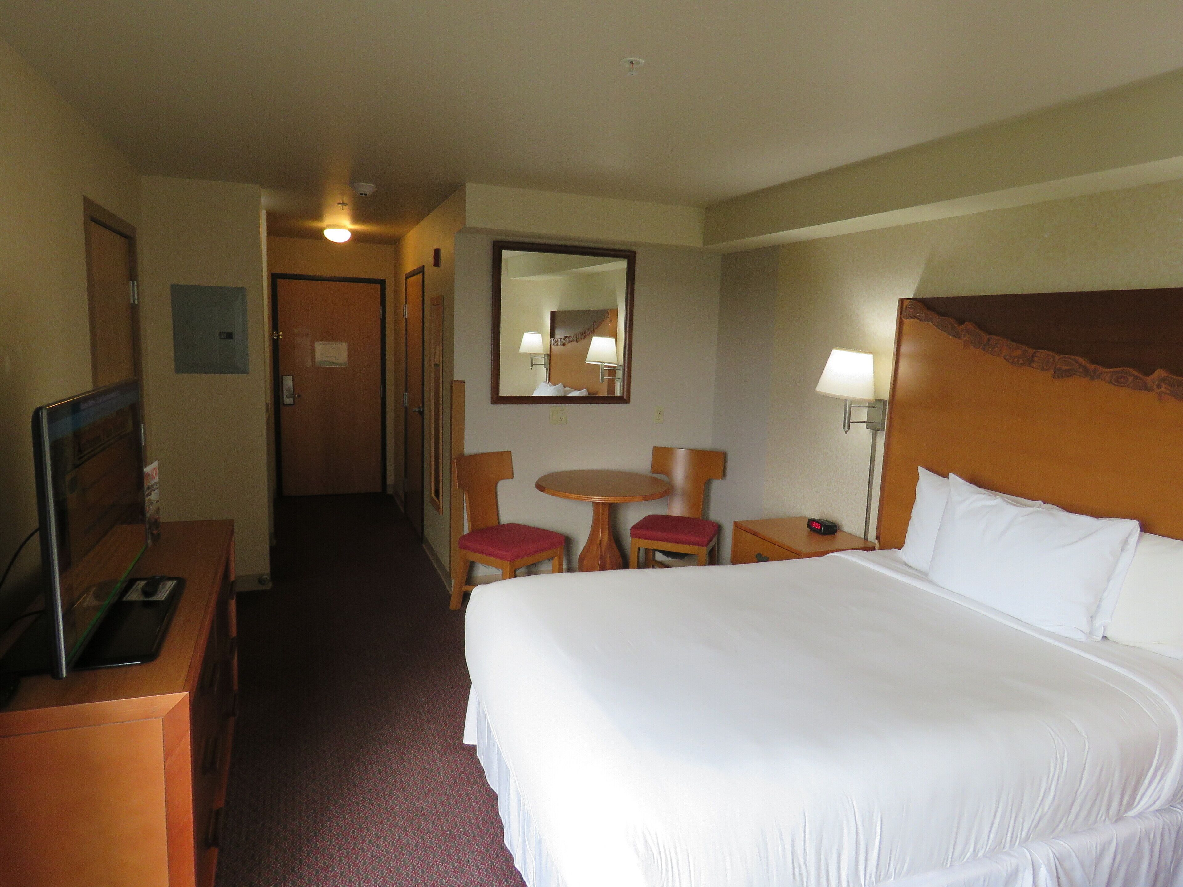 Habitación de hotel con una cama grande, un escritorio con computadora, una silla, una mesita y una lámpara.