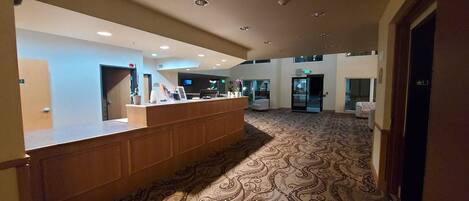 A reception area with a wooden counter, a patterned carpet, and a modern ceiling with recessed lighting.