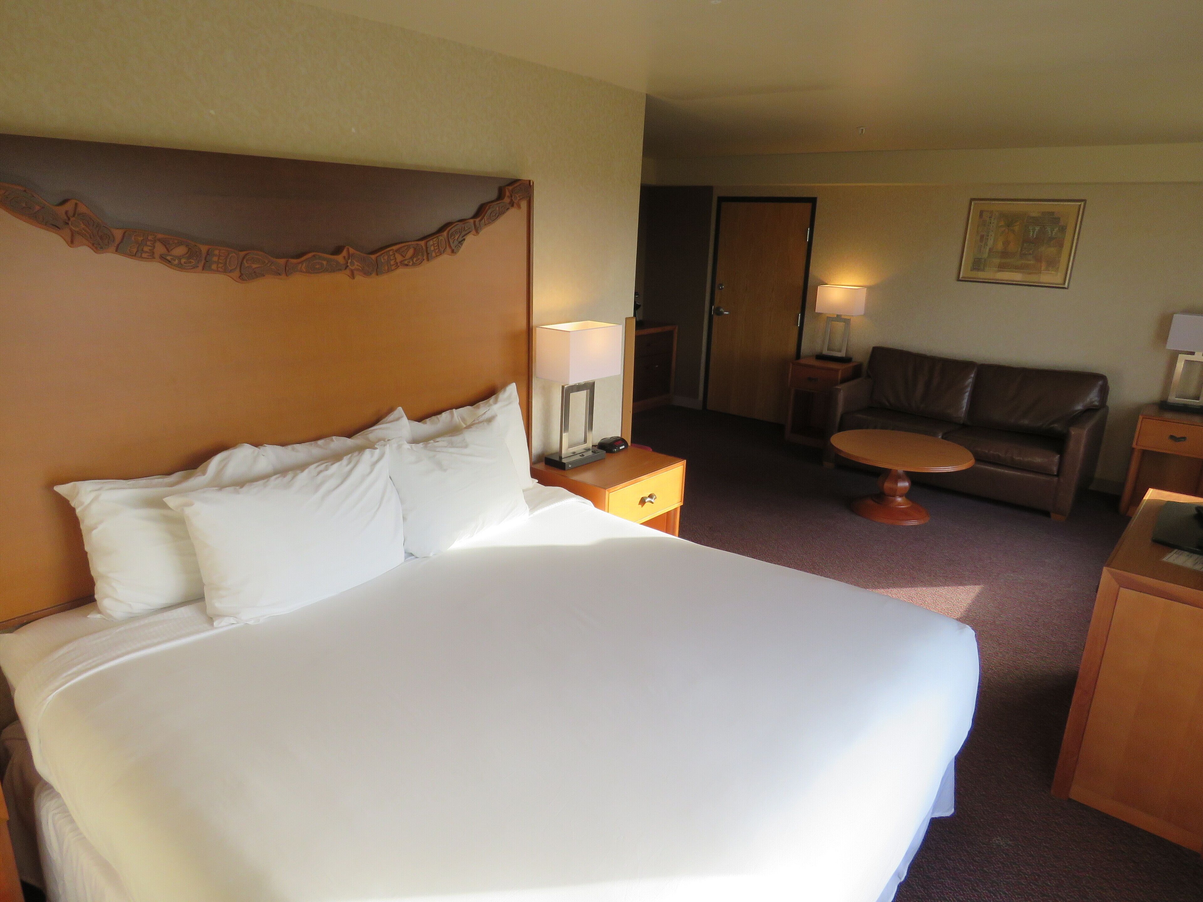A hotel room with a large bed, a wooden headboard, a small table, a sofa, and a door.