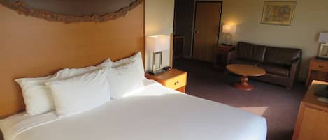 A hotel room with a large bed, a wooden headboard, a small table, a sofa, and a door.
