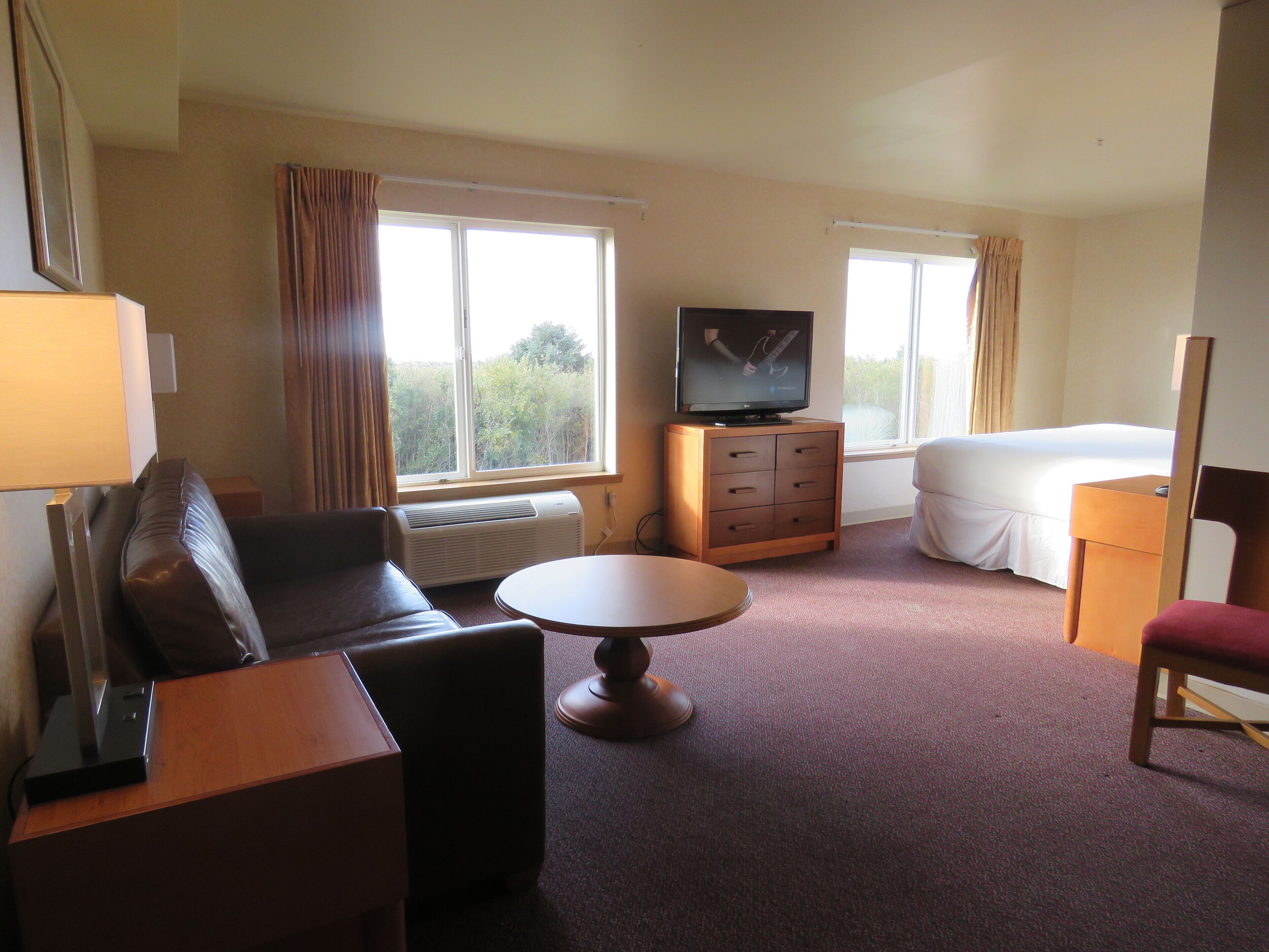 A hotel room with a bed, a TV, a desk, a chair, and a window with curtains.