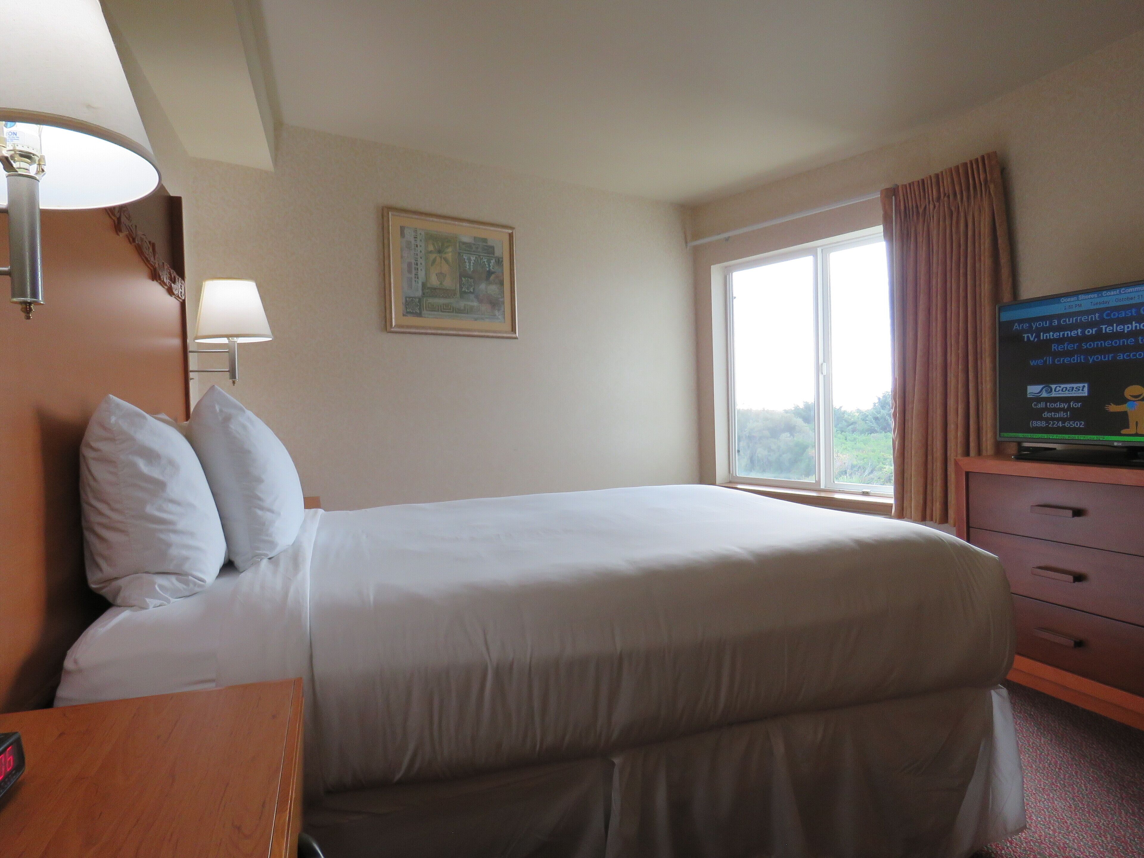 Een hotelkamer met een bed, een bureau, een lamp, een televisie en een raam met gordijnen.
