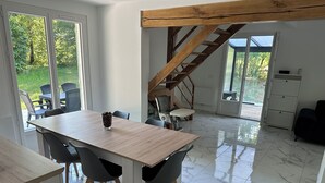 Una cocina moderna con una escalera de madera, un área de comedor con piso de mármol y grandes ventanales con vistas a zonas verdes.