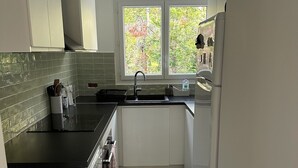 Una cocina moderna con armarios blancos, encimera negra, un lavamanos y una ventana con vistas a árboles.