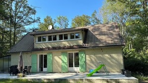 Una casa de dos pisos con techo de tejas, contraventanas verdes y patio de concreto.
