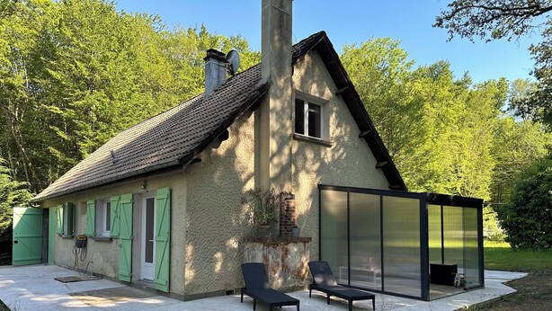 Una casa con chimenea, ventana y un patio con dos sillones y una mesa.