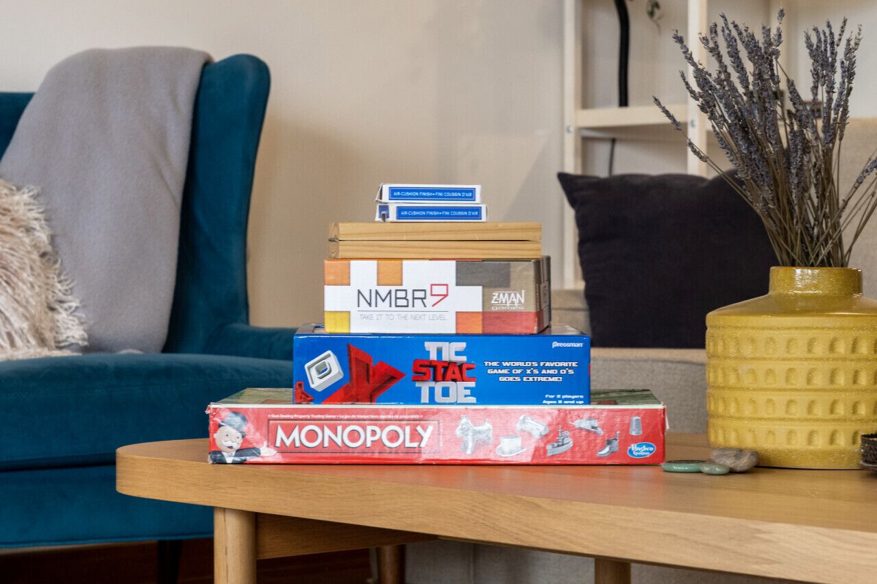 Una sala de estar con un sofá, una mesa de centro y una pila de juegos de mesa, incluyendo Monopoly y otros.
