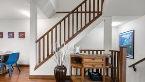 Una escalera con barandillas de madera, un jarrón con ramas, una mesita de madera y un cuadro enmarcado en la pared.
