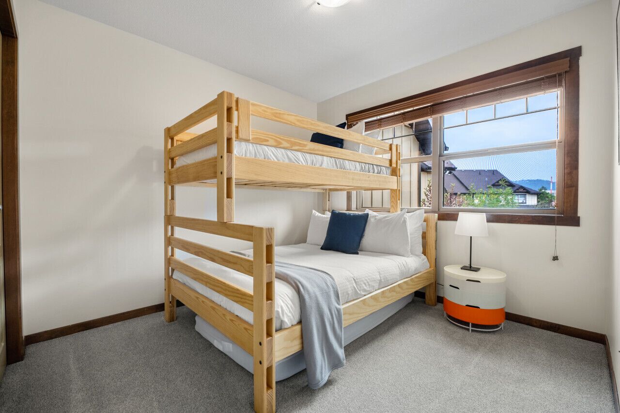 A bunk bed room with a window, a bedside table, and a lamp.