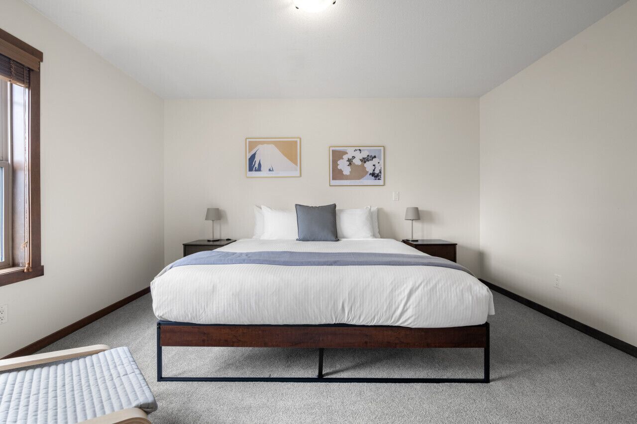 A bedroom with a bed, two bedside tables, a window, and two wall-mounted artworks.