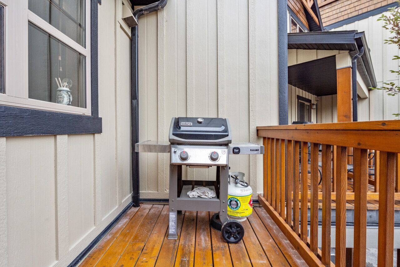 Un barbecue portable sur une terrasse en bois, avec un mur extérieur blanc et une fenêtre.