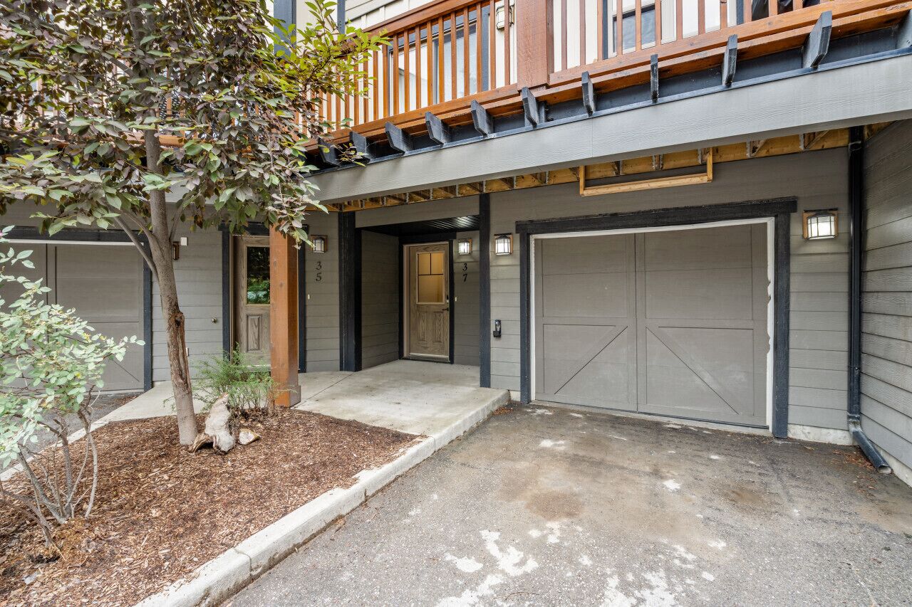 Un bâtiment à deux étages doté d’un porche couvert, de deux portes de garage et d’un petit arbre dans le jardin avant.