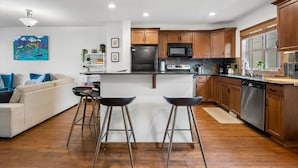 Una cocina moderna con armarios de madera, un refrigerador de acero inoxidable, un microondas y un lavavajillas. Hay una zona con taburetes frente a la isla de la cocina.