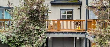 Un immeuble résidentiel de deux étages doté d’un balcon, d’un garage et d’un petit jardin avec un arbre.