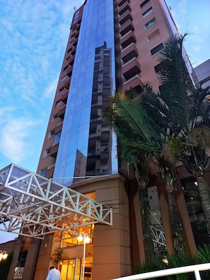 A high-rise building with a glass facade and a white metal structure in front.